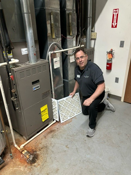 A man kneeling next to a furnace in a room, changing furnace filters.