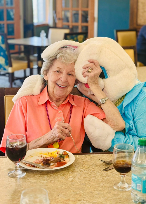 Senior resident shares a joyful hug with someone dressed as the Easter Bunny while enjoying a holiday meal, creating cheerful memories during the celebration.