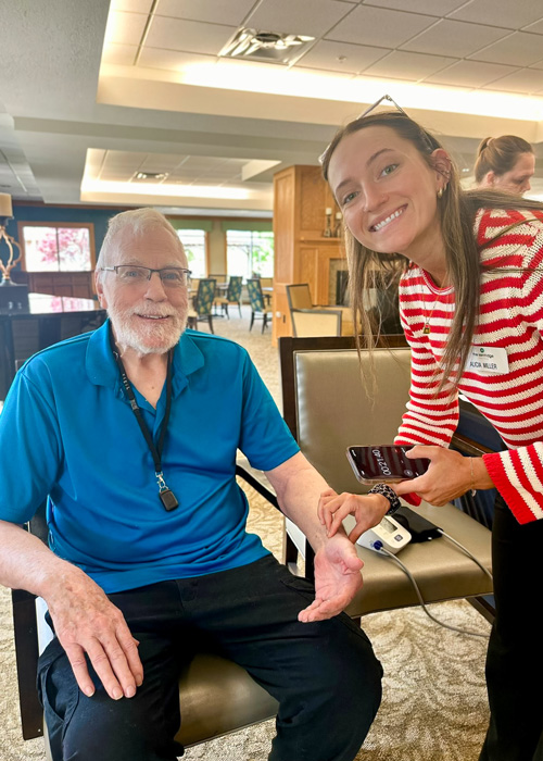 Team member checks a senior resident’s vitals during a Wellness Wednesday event, both smiling and sharing a positive moment focused on health and care.