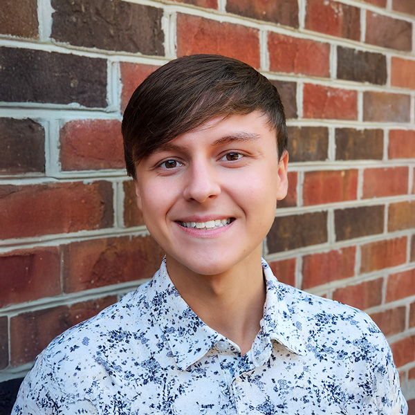 Bryce Gosnick, Memory Care Director at The Kentridge Senior Living, wearing a white patterned button-up shirt, smiling in front of a brick wall.