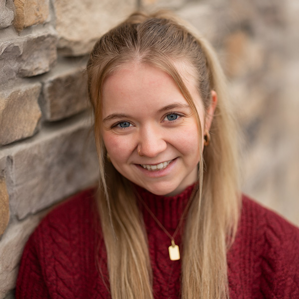 Ariel Jones, Resident Services Director at Kentridge Senior Living, smiling in a burgundy sweater with long blonde hair, standing against a stone wall with a softly blurred background.