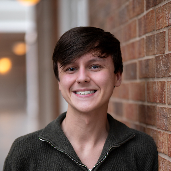Bryce Gosnick, Memory Care Director at The Kentridge Senior Living, smiling in a professional headshot, wearing a green quarter-zip sweater, with a softly blurred brick background.