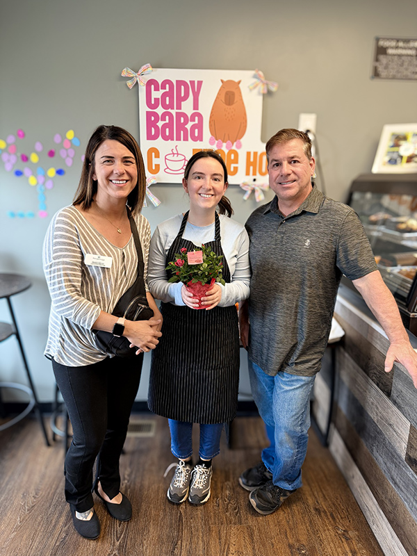 A team member from The KentRidge Senior Living presents a blooming plant to the owners of Capybara Coffee House.