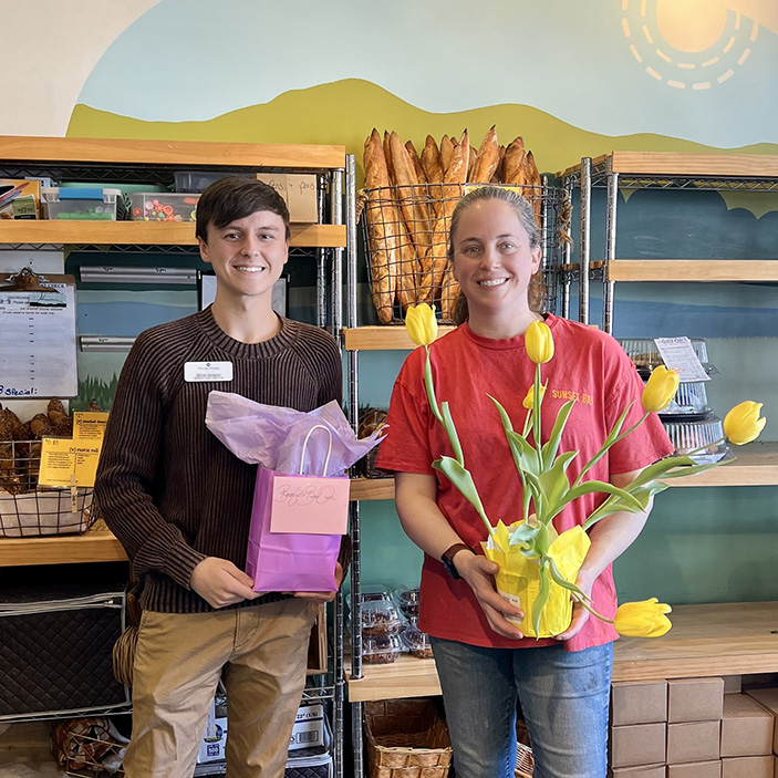 A team member at The KentRidge Senior Living presents a pot of tall yellow flowers to a woman at a local bakery.