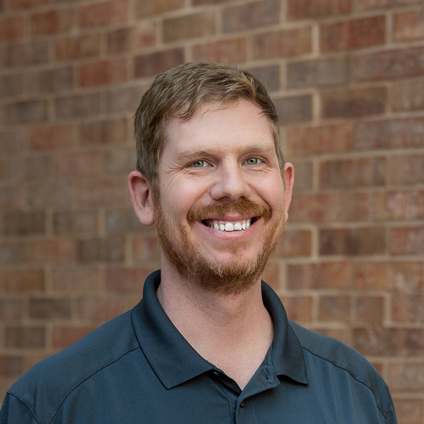 Coby Morehart, Plant Operations Director at The KentRidge Senior Living, smiling in a professional outdoor headshot with short light brown hair, a reddish beard, a dark polo shirt, and a softly blurred brick background.